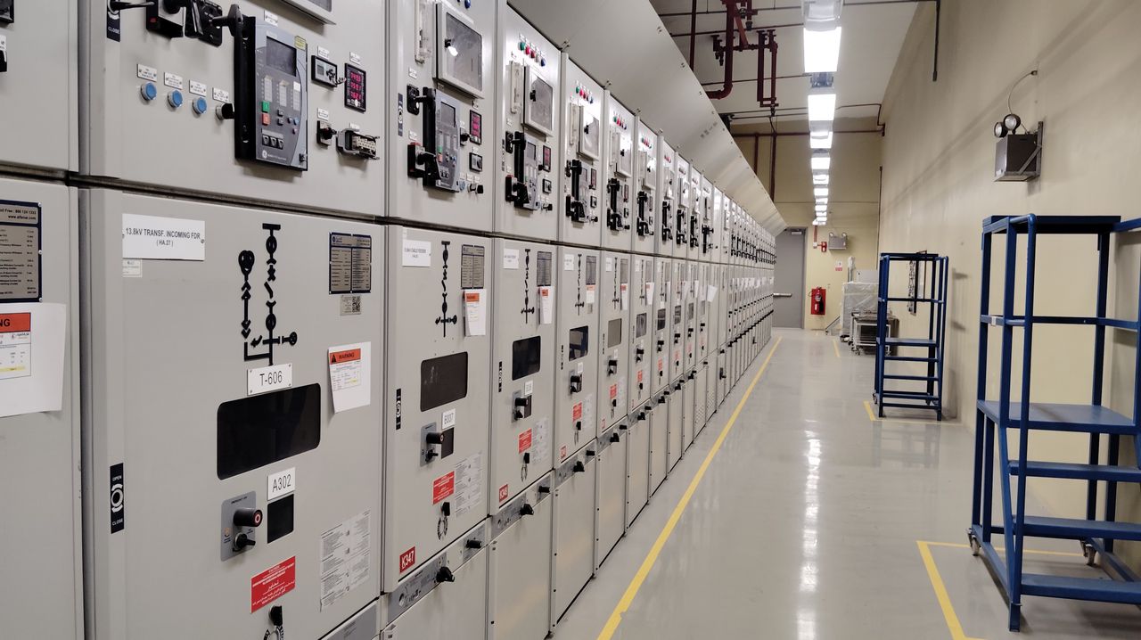 services-02 Long row of control panels in an industrial electrical control room, well-lit and spacious.
